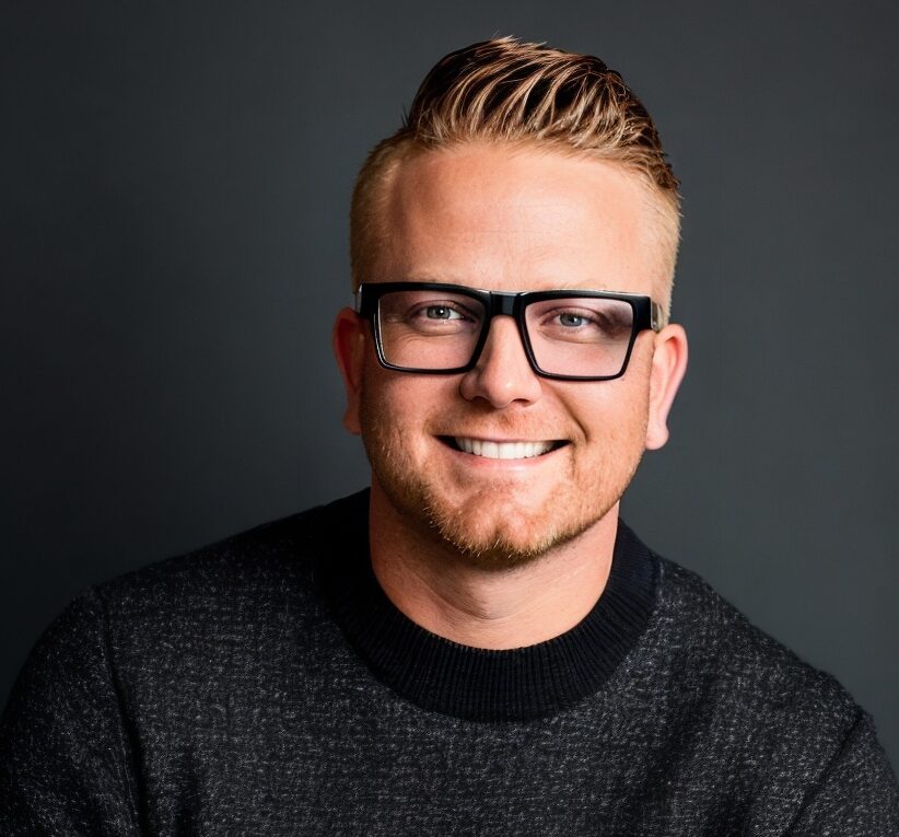 Man in glasses smiling, gray sweater, professional portrait.