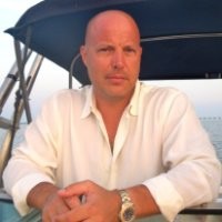 Bald man in white shirt sitting outdoors at sunset